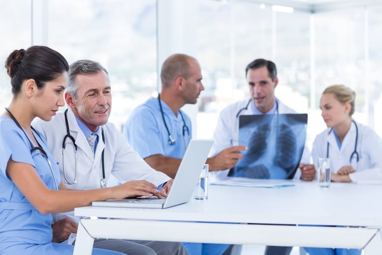 Doctors using computer while their colleagues look at Xray in medical office
