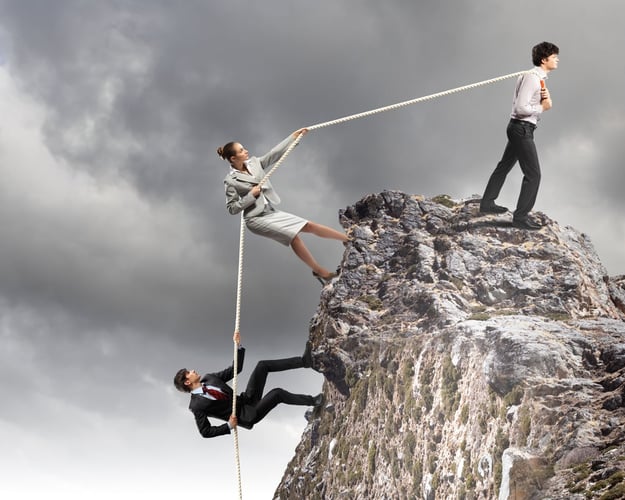 Image of three businesspeople working together to pull rope atop of mountain